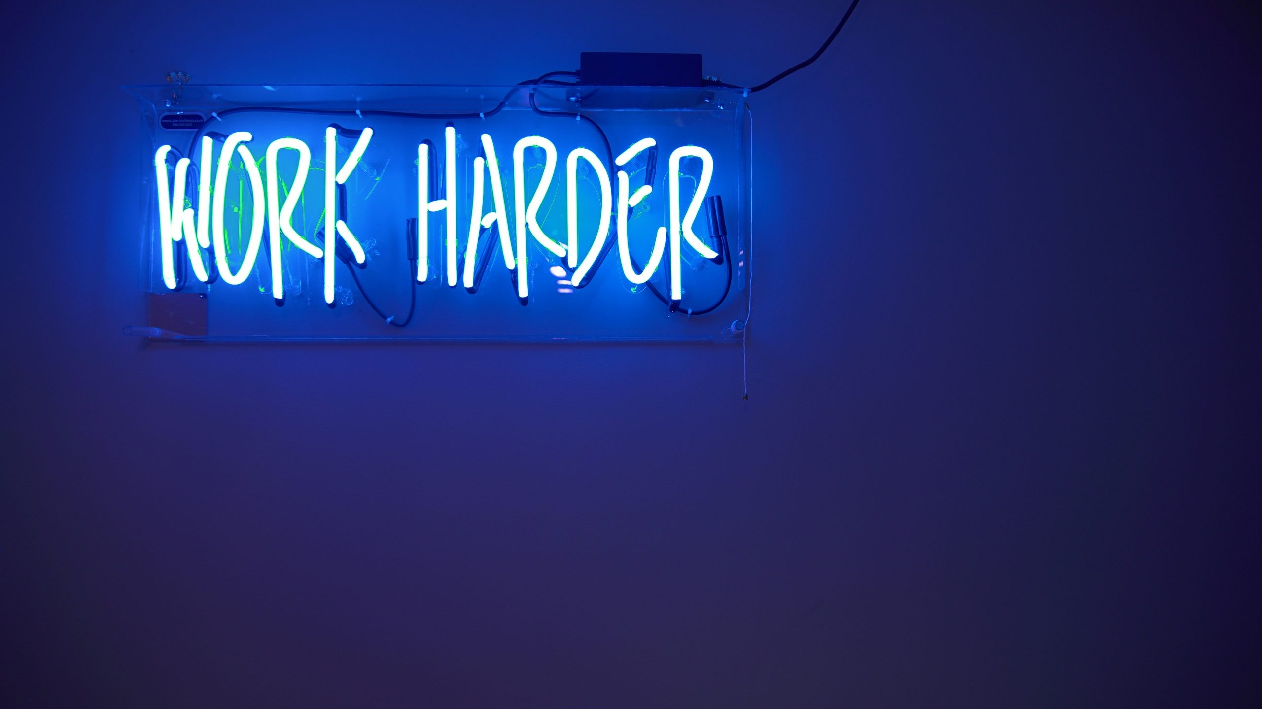 Neon-skilt med teksten "Work Harder" som symboliserer dedikasjon.