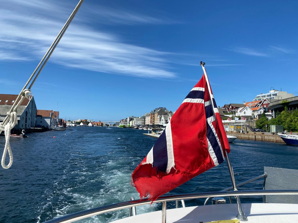 Norsk flagg på en båt med utsikt over en kystby, representerer offentlige tilskudd og støtteordninger i Norge.