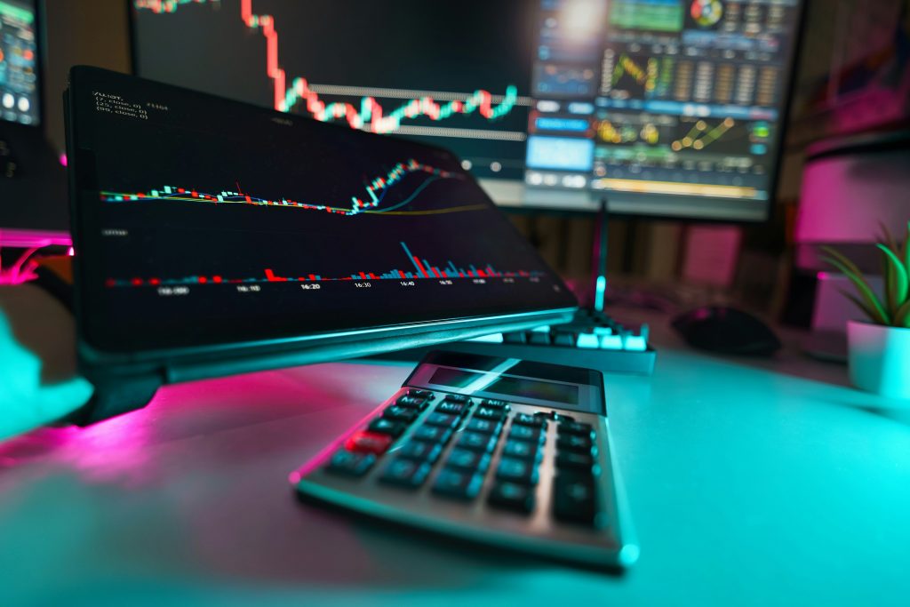 Skjerm med aksjegrafer og kalkulator på skrivebord, som illustrerer økonomisk analyse og factoring for bedrifter.